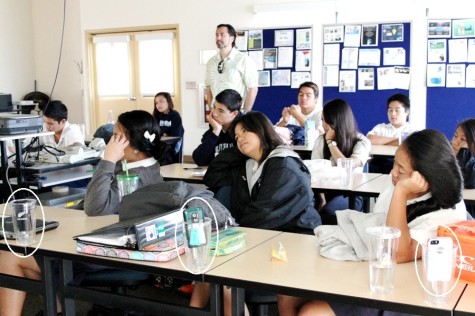 In Mr. Kealii Mossman's class, it isn't enough to be physically present. To make sure they are there mentally as well, Mr. Mossman has students deposit their phones in desktop cups (circled). Other teachers have baskets or boxes to collect cellphones before class starts. Photo by Daisy Draper.